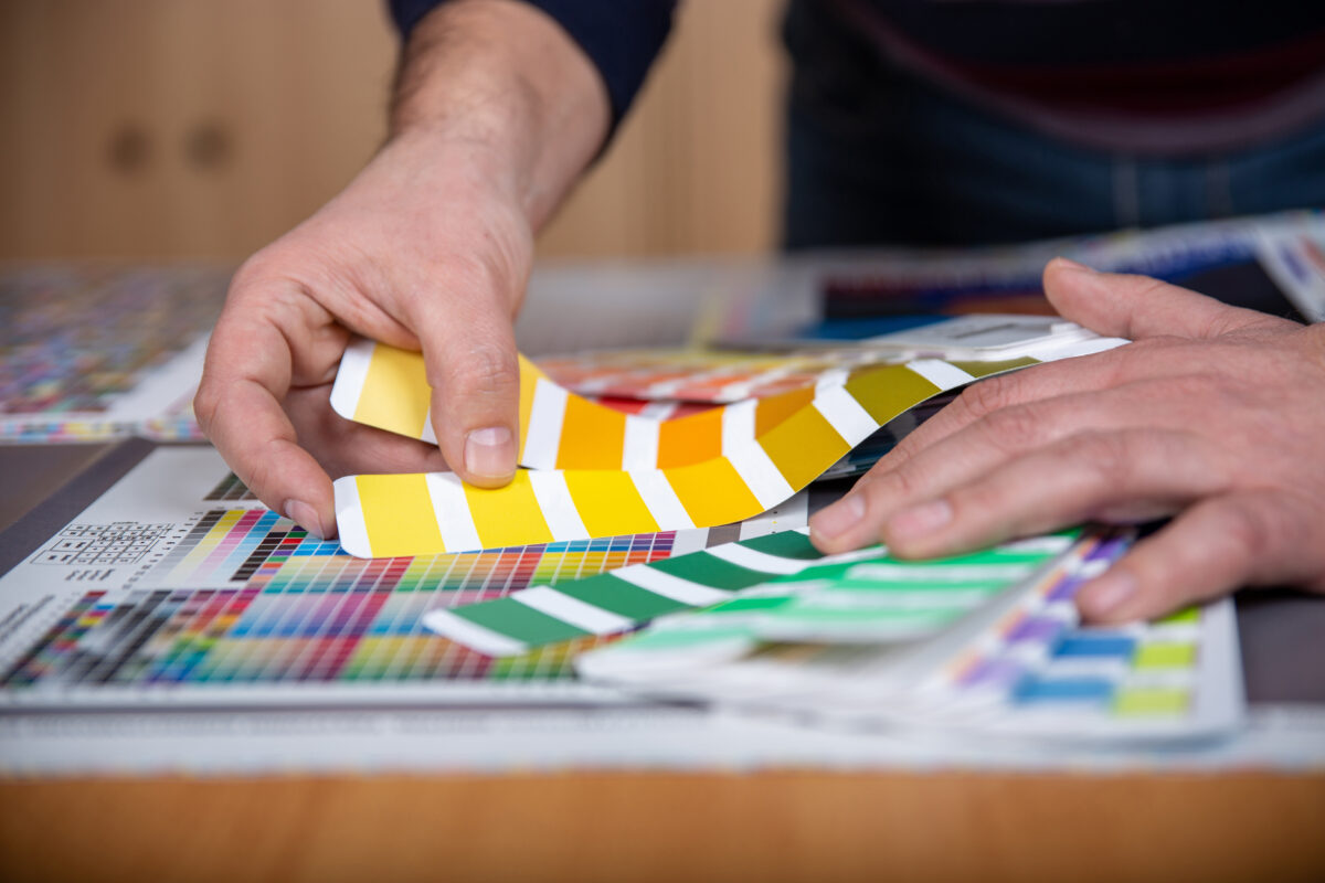 Worker in a printing and press center uses a color palette to select the correct shade of color from CMYK printed sheet