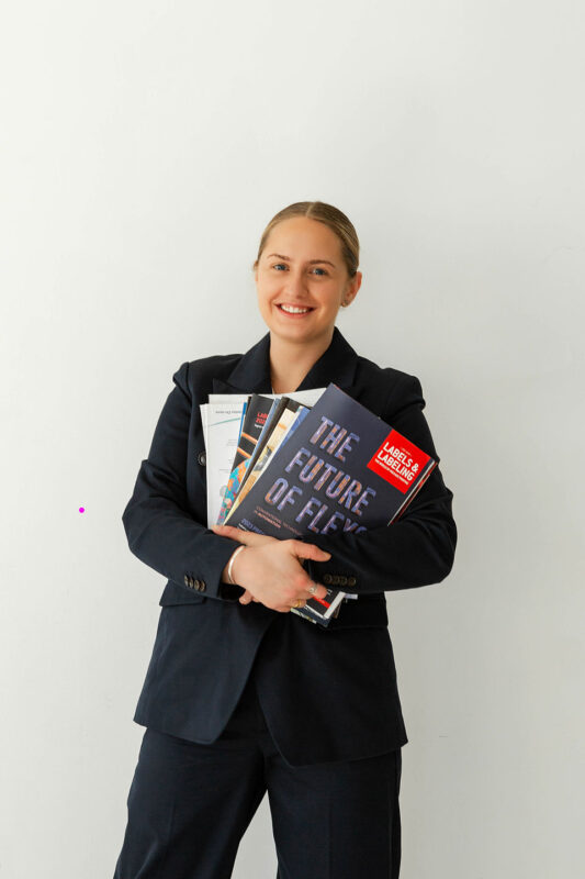 Sales Rep Presenting Corona Treatment Solutions for Flexographic Printing and Labeling - QC Electronics Sales representative with corona treatment solutions for printing and labeling applications holding a stack of flexographic industry magazines.