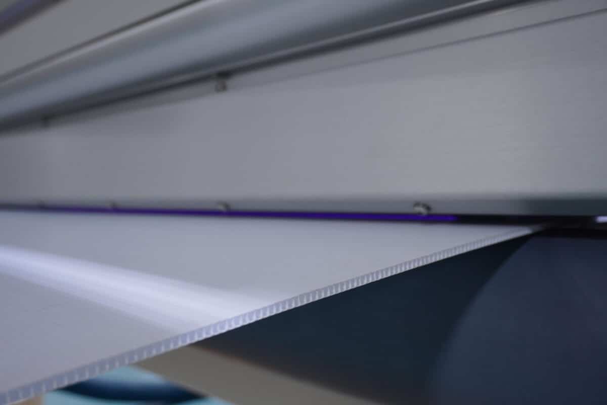QC Electronics C-Series corona treater actively treating corrugated plastic sheet, with the violet corona discharge visible across the electrode gap