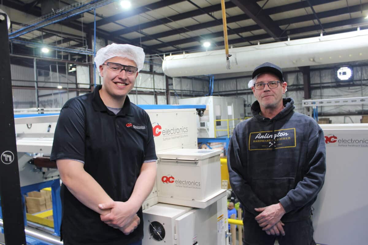 QC Electronics engineer Carl Klein (left) poses with Plant Manager Charlie Smith in front of the company's newly commissioned corona treatment system.