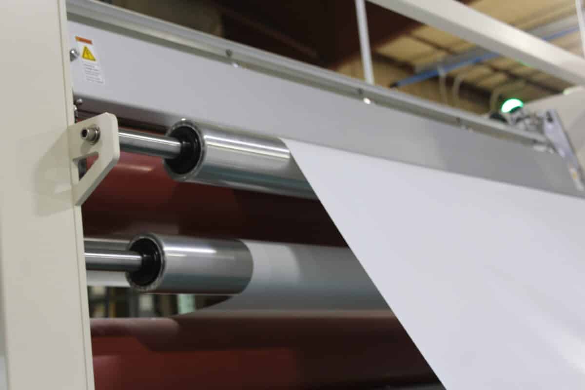 Industrial roller assembly with chrome cylindrical rollers and a light-colored frame; a green indicator light visible in the background.